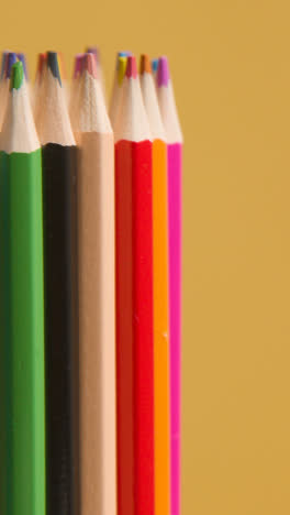 Vertical-Video-Studio-Shot-Of-Rotating-Multi-Coloured-Pencils-Against-Yellow-Background-